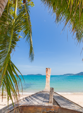 This image shows the luxurious Bang Tao Beach, lined with upscale resorts and beach clubs. Visitors are seen lounging by the resort pools, while others engage in water sports such as parasailing and jet skiing, enjoying a mix of relaxation and adventure.