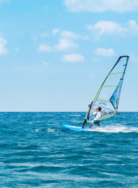 This image shows an exciting windsurfing session in the calm waters of Phuket. The windsurfer skillfully rides the waves, with the tropical landscape in the background, offering a thrilling water sport experience for both beginners and experts.