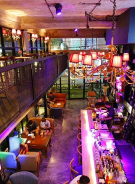 This image shows the unique book-themed interiors of The Library Bar in Old Town Phuket. It highlights bookshelves filled with literary classics, elegant seating arrangements, and patrons sipping cocktails in a warm, inviting environment.