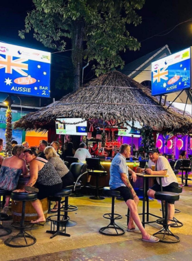 This image shows a sports event at Aussie Bar in Patong, Phuket. It depicts patrons gathered around large screens, cheering and enjoying beers, showcasing the bar’s laid-back and friendly environment for sports enthusiasts.