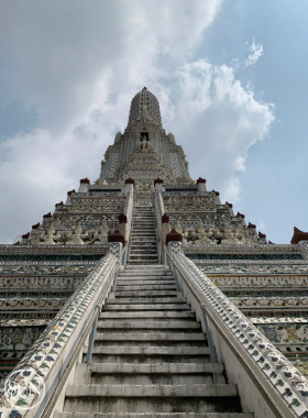 This image shows the majestic Wat Arun in Bangkok, with its intricately designed spires reflecting sunlight. The serene riverside setting and the temple's symmetrical beauty make it an iconic spot for cultural photography.