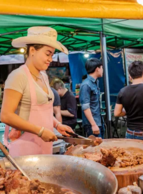 This image shows a plate of Khao Kha Moo, a flavorful braised pork leg served with rice, available at the famous Cowboy Hat Lady’s street food stall in Chiang Mai. The vibrant street scene adds to the local dining experience.