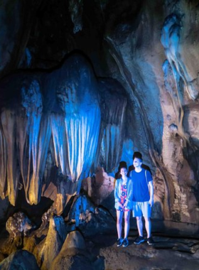 This image shows the entrance to Chiang Dao Caves, surrounded by lush greenery and limestone cliffs. The cave’s natural beauty is accentuated by intricate statues and offerings placed at the entrance. Visitors explore the pathways leading inside, where stalactites and historical relics await. The photo captures the allure of adventure and history in a serene natural setting.