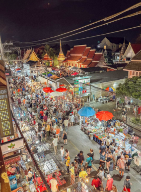 This image shows a vibrant night market in Chiang Mai, bustling with visitors exploring colorful stalls under string lights. Vendors display handcrafted goods, street food, and souvenirs, creating a lively and inviting atmosphere. The aroma of local dishes fills the air as people interact with friendly vendors. The photo captures the cultural richness and energetic vibe of this must-visit attraction.