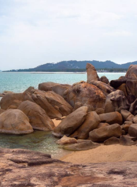 This image shows Hin Ta Hin Yai Market near the iconic Grandfather and Grandmother Rocks in Koh Samui. It highlights the variety of snacks, such as spicy sausages and refreshing coconut ice cream, enjoyed in a casual and scenic tropical setting.