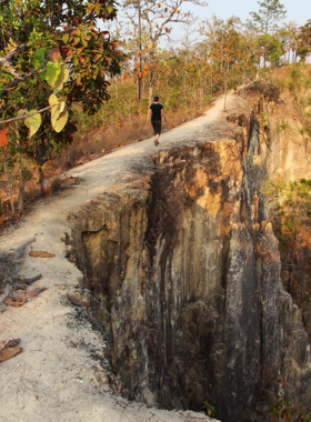 This image shows Pai Canyon, a natural landscape with red, rugged ridges, narrow pathways, and breathtaking views of the valley below. Visitors can walk along the elevated trails, experiencing the beauty of Pai's countryside and the surrounding forest. The bright blue sky and golden hour sunlight create a stunning backdrop, making it a perfect spot for photography and nature lovers.