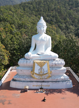 This image shows the Big Buddha statue located on a hill in Pai, towering above the landscape. Visitors climb the 353 steps to reach the statue, where they can enjoy panoramic views of Pai's countryside. The statue is white and majestic, set against a backdrop of lush green mountains. This tranquil spot offers visitors a peaceful experience and spiritual reflection.