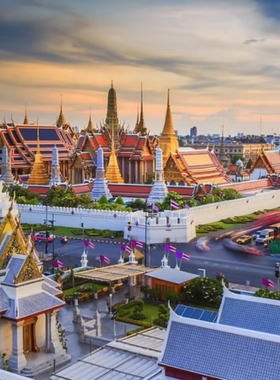 This image shows the grandeur of the Grand Palace in Bangkok, Thailand. The majestic palace is surrounded by intricate golden architecture and lush greenery, representing Thailand's rich royal history and culture.