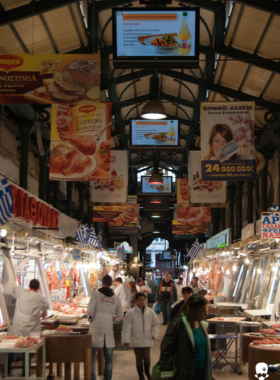 This image shows the Varvakios Agora market, a bustling spot in Monastiraki, Athens. The market offers a sensory experience with local vendors selling fresh meat, fish, spices, and produce. The vibrant atmosphere, especially in the early morning, reflects authentic local culture.