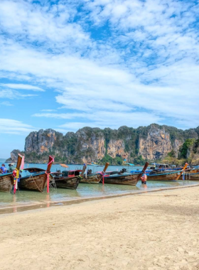 This image shows an adventurous traveler rock climbing at Railay Beach in Krabi, Thailand. The towering limestone cliffs provide a thrilling challenge for climbers while offering stunning views of the turquoise sea below.