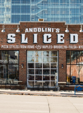 This image shows a freshly baked pizza at Andolini’s Pizzeria, topped with fresh ingredients and served on a rustic wooden table.