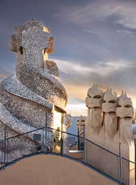 This image shows the rooftop of Casa Milà (La Pedrera), designed by Antoni Gaudí, with its unique, organic chimneys and views over the city. The undulating stone facade and whimsical design make it one of Barcelona's most visited landmarks.