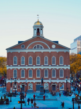 This image shows Faneuil Hall Marketplace in Boston, a bustling area filled with historic charm, shops, restaurants, and street performances. The hall is a beautiful colonial building surrounded by visitors enjoying the lively atmosphere, showcasing how history blends with modern culture here.