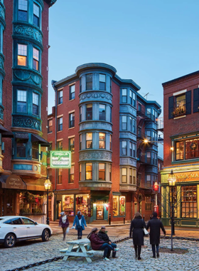 This image shows the North End neighborhood in Boston, known for its Italian heritage, cobblestone streets, and historic landmarks. Vibrant cafes and authentic Italian restaurants line the streets, with visitors enjoying delicious food and the area’s cultural charm.