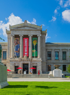 This image shows the grand Museum of Fine Arts in Boston, showcasing its impressive neoclassical architecture. The museum is surrounded by greenery, with visitors admiring exhibits that range from ancient artifacts to modern masterpieces in this world-renowned cultural institution.