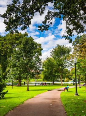 This image shows Boston Common, the oldest public park in the United States, with wide-open green spaces, tall trees, and families relaxing under the shade. It highlights the park's tranquil beauty and its role as a community gathering place.