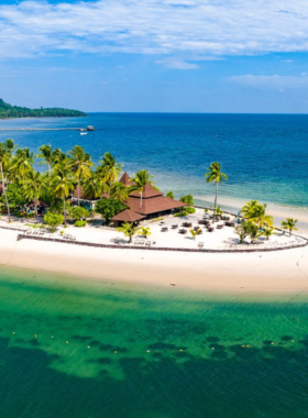 This image shows the serene Garnet Beach, also called Charlie Beach, with soft white sands and crystal-clear turquoise waters surrounded by lush greenery. A few visitors are seen relaxing under the sun while enjoying the tranquil beach vibe.

