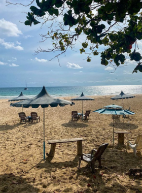 This image shows Rajamangala Beach, a long stretch of white sand with crystal-clear waters under the bright sun. The setting is perfect for relaxation, as families and individuals are seen enjoying the pristine beauty of the beach.