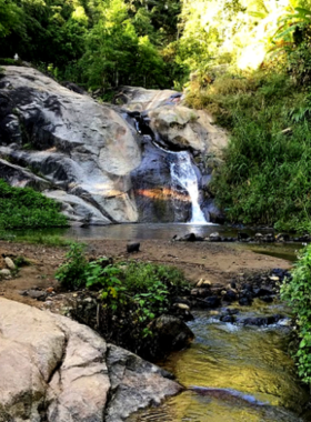 This image shows the serene Mor Paeng Waterfall in Pai, Thailand, with water flowing gently over smooth rocks into natural pools surrounded by lush greenery.