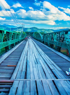 This image shows Pai Memorial Bridge illuminated softly at night in Thailand, offering a quiet and atmospheric experience with reflections shimmering on the nearby water.