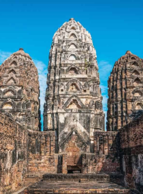 This image shows the serene beauty of Sukhothai Historical Park during sunset, with the golden hues reflecting off ancient ruins and peaceful ponds. The historical temples and majestic Buddha statues are bathed in soft, warm light, creating a tranquil atmosphere for visitors to enjoy the rich history and natural surroundings.