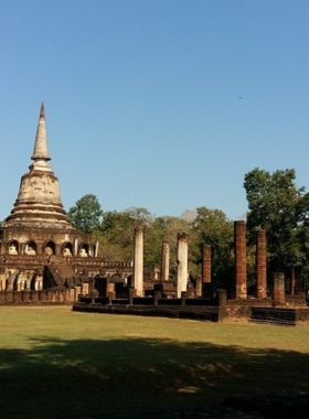 This image shows the unique Wat Chang Lom temple, featuring sculpted elephants around the base of the chedi. The peaceful surroundings, including trees and open fields, make it a perfect spot for visitors to admire the architecture and historical significance of the Sukhothai period.