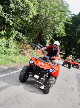 This image shows an exciting ATV adventure in Ayutthaya, where tourists ride through rugged trails, ancient ruins, dense jungle, and small local villages, offering a thrilling exploration of the historical city. The terrain is challenging yet beautiful, providing an adrenaline-packed experience for adventure seekers of all levels. The landscape features a mix of old temples and lush greenery, with the ATV speeding along the paths less traveled.