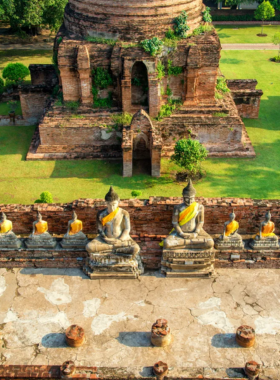 This image shows the ancient ruins of Ayutthaya Historical Park, including tall temple spires and weathered brick structures surrounded by lush greenery. The peaceful atmosphere highlights the harmony between history and nature, making it an iconic location for photography.
