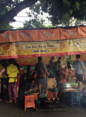 This image shows the bustling street food stall of Sate Babi Bawah Pohon in Kuta, Bali. The skewers of marinated pork are grilled over charcoal, creating a smoky and flavorful street food experience. Locals and tourists alike gather here to enjoy this authentic Balinese dish.
