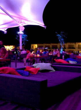 This image shows Velvet & Hypnotized, a chic rooftop bar in Bali offering panoramic views of Denpasar. Guests are seen relaxing with drinks, enjoying the cityscape, and listening to live music in a stylish and breezy setting.