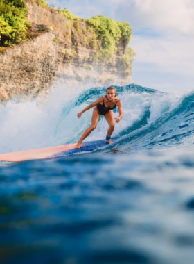 This image shows a surfer riding a wave at Batu Bolong Beach in Canggu, Bali. The clear blue ocean, sunny skies, and a backdrop of other surfers waiting for their turn add to the vibrant and adventurous atmosphere of this popular surfing destination. The image highlights the thrill of surfing, the beauty of Bali’s coastal landscape, and the active lifestyle that draws both beginners and experienced surfers to the area.
