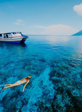 11. Nusa Penida Snorkeling Adventure This image shows the vibrant underwater world of Nusa Penida during a snorkeling trip. The crystal-clear waters reveal colorful coral reefs teeming with tropical fish of various shapes and hues. A snorkeler is seen gliding effortlessly, immersed in the beauty of the ocean. The scene exudes tranquility and adventure, showcasing the rich marine biodiversity that makes Nusa Penida a dream destination for water enthusiasts and nature lovers alike.