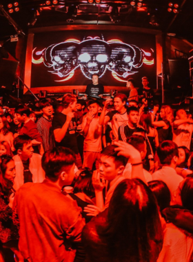 This image shows Hero Club in Hanoi with its futuristic neon lighting and high-energy dance floor. The lively atmosphere is depicted with a crowd of partygoers, pulsing music, and a DJ at the center of the action.