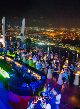 This image shows SKY36 rooftop bar in Da Nang with its luxurious setup and breathtaking views. The photo captures the glowing cityscape, chic seating arrangements, and guests enjoying drinks under a star-lit sky.