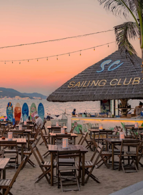 This image shows Sailing Club in Nha Trang, a beach club offering a mix of relaxation and nightlife. The photo highlights its sandy beachfront, guests enjoying cocktails under the stars, and lively fire show performances.