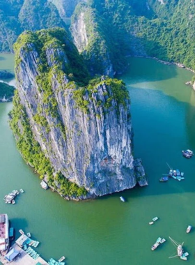 This image shows the iconic emerald waters of Halong Bay, dotted with towering limestone islands and small boats cruising through the serene scenery. The golden sunset casts a magical glow over the bay, capturing its tranquil beauty and making it a favorite spot for travelers and photographers.