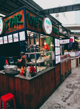 This image shows the lively and bustling Ben Thanh Street Food Market, with vibrant food stalls offering a variety of dishes like pho, banh xeo, and fresh sugarcane juice. The communal seating and colorful ambiance capture the energy of Saigon’s street food culture.