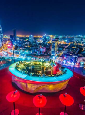 This image shows Chill Skybar in Ho Chi Minh City, a famous rooftop bar with stunning panoramic views of the city skyline. You can see colorful lights from the bar illuminating the modern outdoor seating and the vibrant cityscape below. The atmosphere is chic and upscale, with patrons enjoying cocktails under the open sky. This rooftop venue captures the lively yet elegant vibe of Saigon’s nightlife, making it a perfect spot for sunsets and nighttime entertainment.