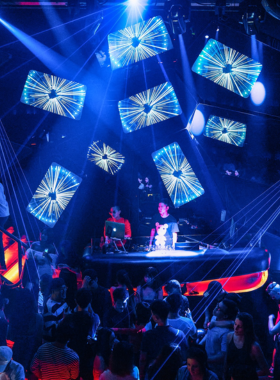 This image shows Lush Nightclub in Ho Chi Minh City, a vibrant and modern party venue. Neon lights and colorful decorations fill the space, with a lively dance floor full of people. A DJ is spinning tracks, and the crowd is dancing energetically. The atmosphere is electric, with loud music and a mix of locals and travelers enjoying the night. Tables with drinks and stylish seating areas are visible, showing the club's energetic yet upscale vibe.