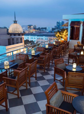 This image shows Saigon Saigon Rooftop Bar, a historic rooftop venue with colonial-style decor. You can see elegant wooden furniture and live jazz performers creating a classic vibe. Patrons are enjoying cocktails while overlooking the bustling streets of Ho Chi Minh City from above. The nighttime view of the city is stunning, with bright lights and a relaxed ambiance. The vintage charm of this bar makes it an ideal spot for unwinding in a timeless setting.