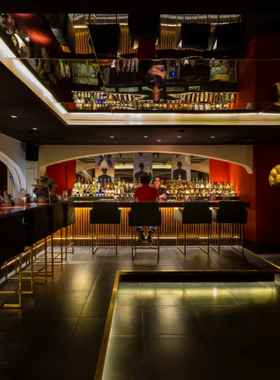 This image shows Rabbit Hole, a speakeasy bar in Ho Chi Minh City known for its intimate and classy vibe. The bar is dimly lit, with plush seating and a well-stocked bar in the background. A bartender is seen preparing a creative cocktail with flair. The setting feels exclusive and sophisticated, with stylish decor and cozy corners perfect for private conversations. The warm lighting adds to the charm, making it a great place for cocktail enthusiasts.