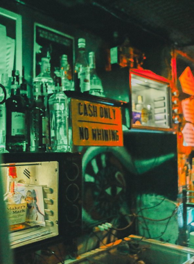 This image shows TNR Saigon, a dive bar in Ho Chi Minh City with a relaxed and fun-loving atmosphere. The walls are covered in graffiti and posters, giving it an edgy and youthful vibe. People are seen enjoying drinks at the bar counter while a live band performs in the corner. The seating is casual, with a mix of locals and travelers socializing. The overall setting is vibrant and laid-back, perfect for an affordable and energetic night out.