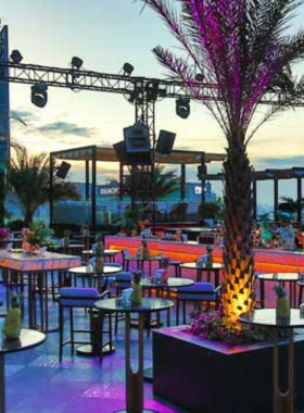 This image shows Sky XX Garden & Lounge, a luxurious rooftop bar in Ho Chi Minh City. The setting features elegant seating with a mix of indoor and outdoor areas overlooking the city skyline. Guests are dressed stylishly, enjoying premium cocktails under soft lighting. The DJ booth and modern décor create a glamorous and chic vibe. The city lights in the background add to the sophisticated atmosphere, making it a perfect venue for upscale nightlife and celebrations.