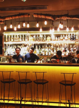 This image shows Corked Tales, a cocktail bar in Ho Chi Minh City known for its artistic and innovative drinks. The bartender is carefully crafting a cocktail with unique garnishes, and the presentation is as impressive as the taste. The bar is cozy and intimate, with dim lighting and comfortable seating. Patrons are seated in small groups, sipping colorful cocktails and enjoying conversations. The warm and creative ambiance makes it a must-visit spot for cocktail enthusiasts.