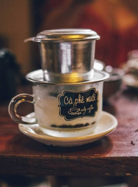 This image shows that Hue is famous for its unique salt coffee, a delightful drink that combines the bitterness of Vietnamese coffee with the sweetness of condensed milk and a pinch of salt. The coffee cup is served with a rich and creamy texture, and it offers a taste that is bold and unforgettable. The setting in the image highlights the relaxed and cozy vibe of a local coffee shop, where this traditional drink is often enjoyed by locals and travelers alike.