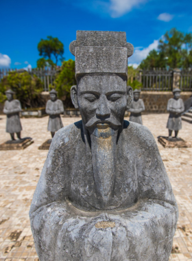 This image shows that Hue is home to several royal tombs, which are grand architectural sites honoring the emperors of the Nguyen Dynasty. The tomb in the image features beautifully crafted stone statues, intricate carvings, and a tranquil garden setting. Visitors can see the peaceful surroundings, which add to the solemn and majestic atmosphere. The image emphasizes how these tombs are both historical landmarks and serene places to learn about Vietnam’s royal history.