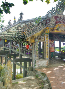 This image shows that the Thanh Toan Tile Bridge is a charming historic structure surrounded by rice fields and streams in the Hue countryside. The bridge in the image features its intricate wooden design and tiled roof, making it a beautiful spot for photography. Visitors walking across the bridge can experience the peaceful and quiet rural atmosphere, offering a refreshing escape from the busy city life of Hue.