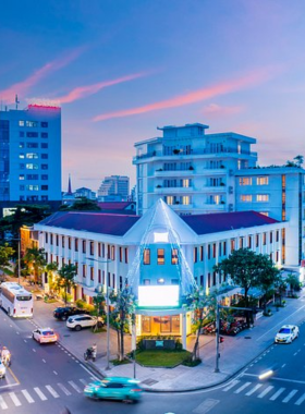 This image shows the vibrant EMM Hotel Hue, a modern and stylish hotel located in the heart of Hue City. The picture highlights its sleek architecture, a beautiful outdoor swimming pool surrounded by lounge chairs, and a cozy seating area that provides a relaxing vibe. It is designed for travelers looking for a comfortable stay while exploring Hue’s cultural and historical sites. The warm and inviting atmosphere makes it an ideal choice for families, couples, and solo travelers.