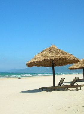  This image shows Thuan An Beach in Hue, Vietnam, on a sunny day. The beach features golden sands stretching along the shoreline with calm blue waters and a clear sky. Visitors can be seen enjoying the peaceful atmosphere, with small fishing boats anchored nearby, enhancing the coastal charm. The tranquil setting makes it a perfect destination for relaxation and nature lovers looking for a serene escape.