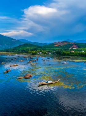 This image shows Tam Giang Lagoon during sunset in Hue, Vietnam. The calm waters reflect the golden and orange hues of the sky, creating a mesmerizing mirror effect. Traditional fishing boats and nets are visible, adding cultural charm to the tranquil scene. The lagoon is surrounded by greenery, making it a peaceful retreat for nature lovers and photographers.